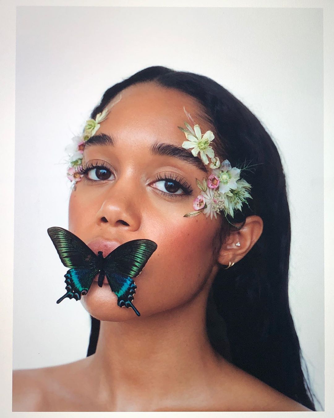 Portrait of a woman with flowers in her hair and a large butterfly on her lips in a beauty and fashion style studio shot.