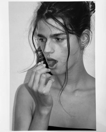 Black and white portrait of a woman with dark hair eating a cherry, photographed by Angelo Pennetta.