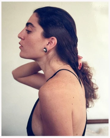 Profile portrait of a woman with dark hair tied back wearing a black top and a round earring, photographed by Angelo Pennetta.