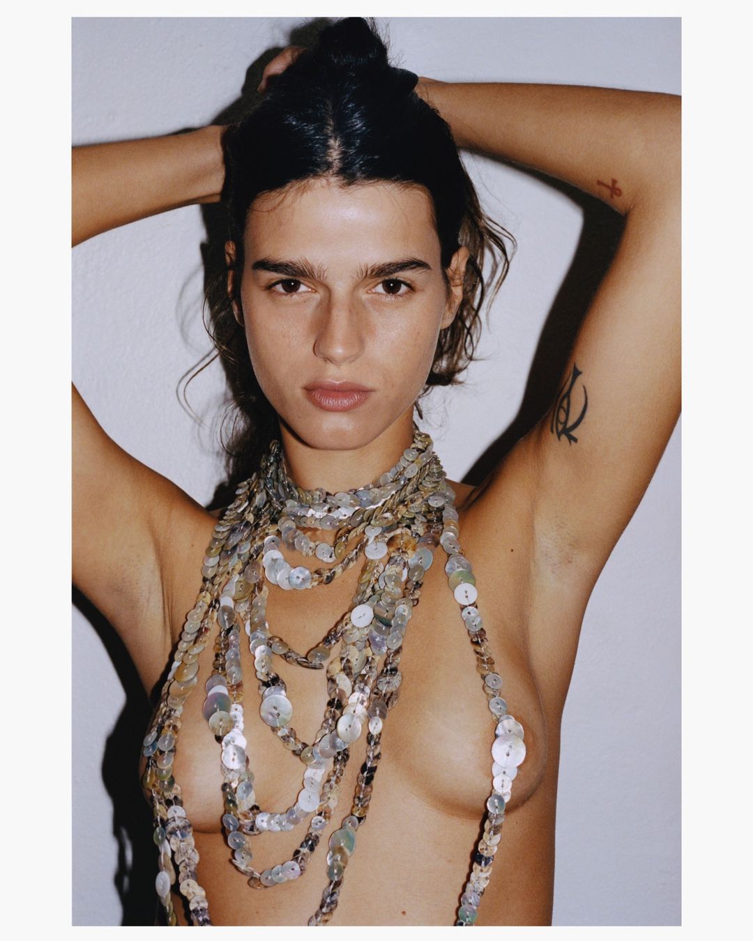 Woman with arms raised wearing a layered button necklace against a white background