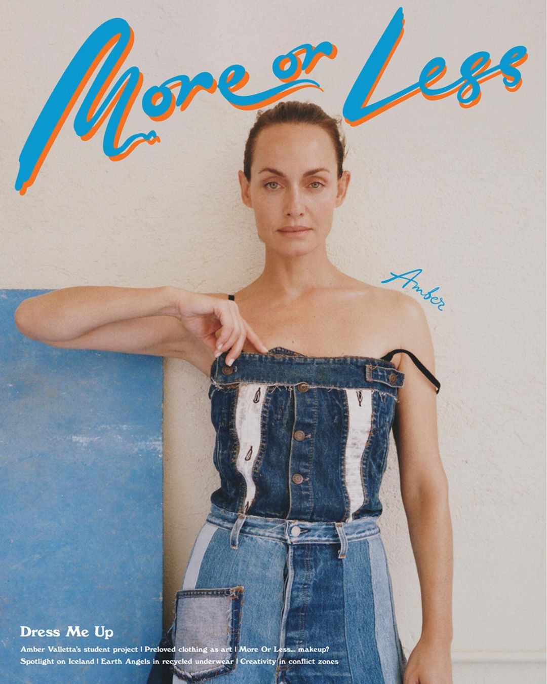 Amber Valletta poses in a denim outfit in front of a blue panel and white wall with More or Less magazine title, shot in portrait.