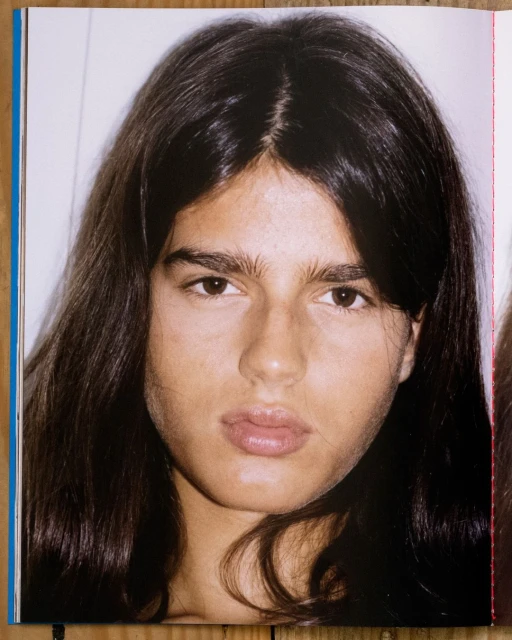 Close-up portrait of a young adult with long dark hair and light skin against a white background, showcasing editorial photography style.
