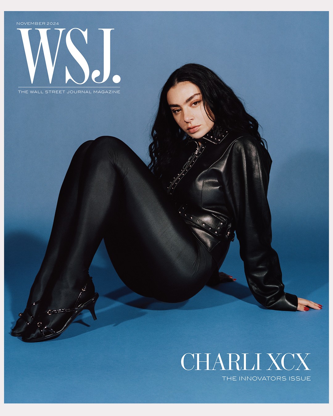 Charli XCX poses in a black leather-like outfit, seated against a light blue backdrop, for WSJ. Magazine's November 2024 cover.
