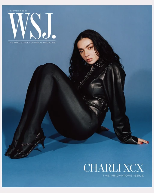 Charli XCX poses in a black leather-like outfit, seated against a light blue backdrop, for WSJ. Magazine's November 2024 cover.