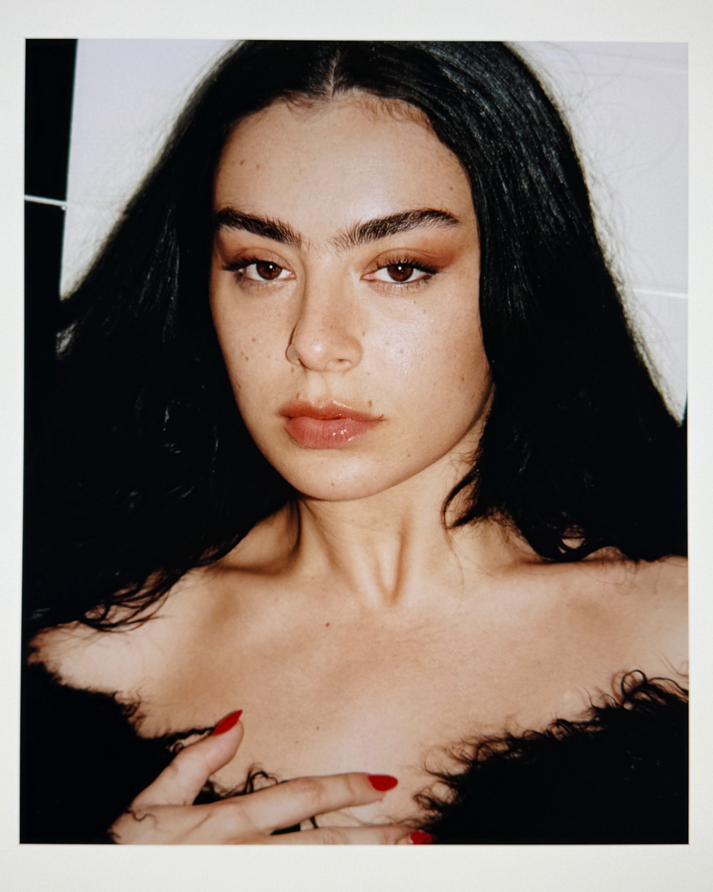 Close-up portrait of an adult female with dark hair and red nail polish, posing with a neutral facial expression against a plain backdrop.