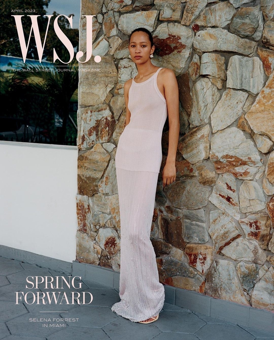 WSJ. magazine cover featuring a woman in a pink dress posing in front of a stone wall, with text overlay and a glimpse of a tropical landscape.