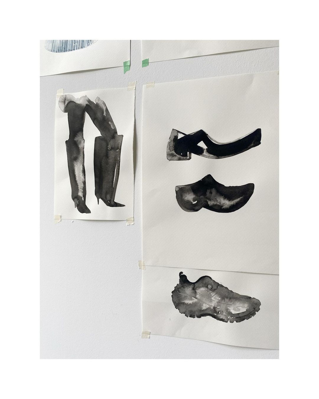 Black ink drawings of various shoe styles, including boots, heels, and sneakers, taped to a white wall, creating a minimalist display.