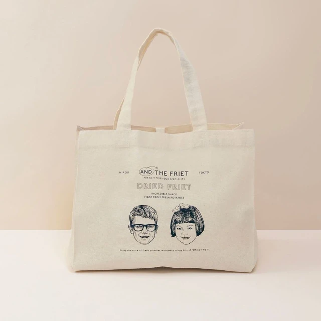 Tote bag on a neutral background features line drawings of a boy and girl, along with the words 'AND THE FRIET DRIED FRIET'.