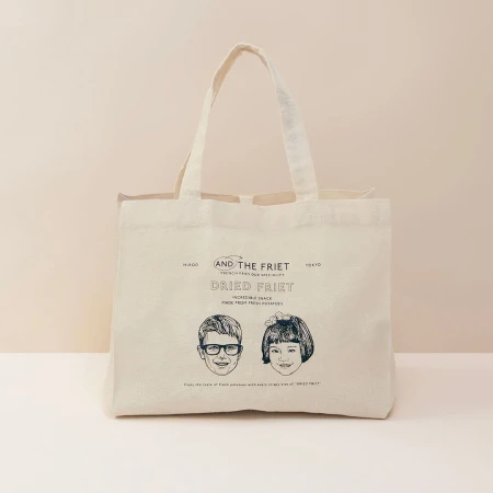 Tote bag on a neutral background features line drawings of a boy and girl, along with the words 'AND THE FRIET DRIED FRIET'.