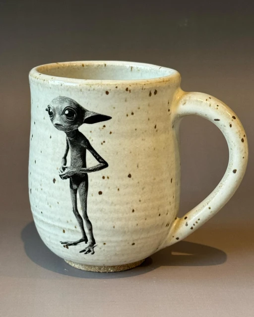 Speckled ceramic mug featuring an illustration of a skinny alien-like figure standing on its own against a neutral backdrop.