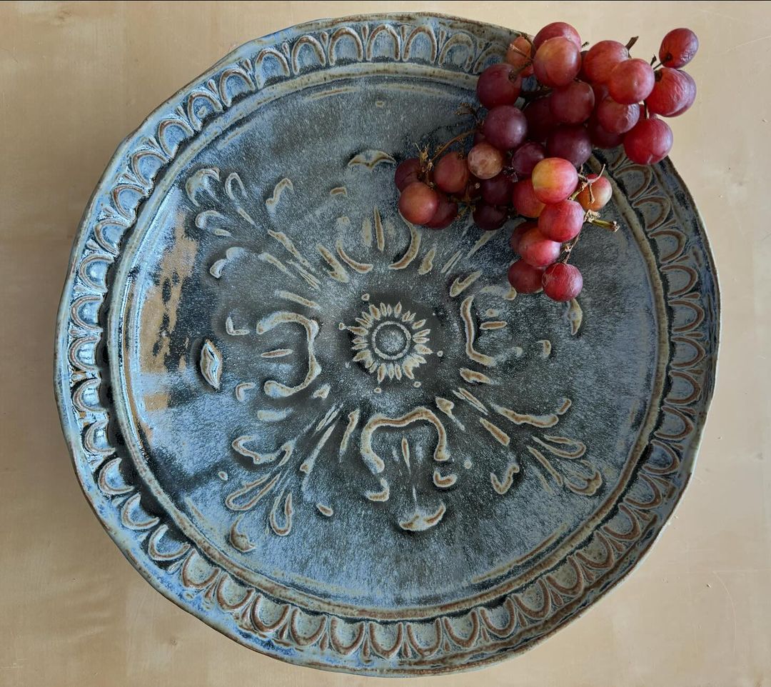 Artisan-crafted plate with ornate floral design, paired with a vibrant bunch of red grapes, creates a sophisticated food presentation.