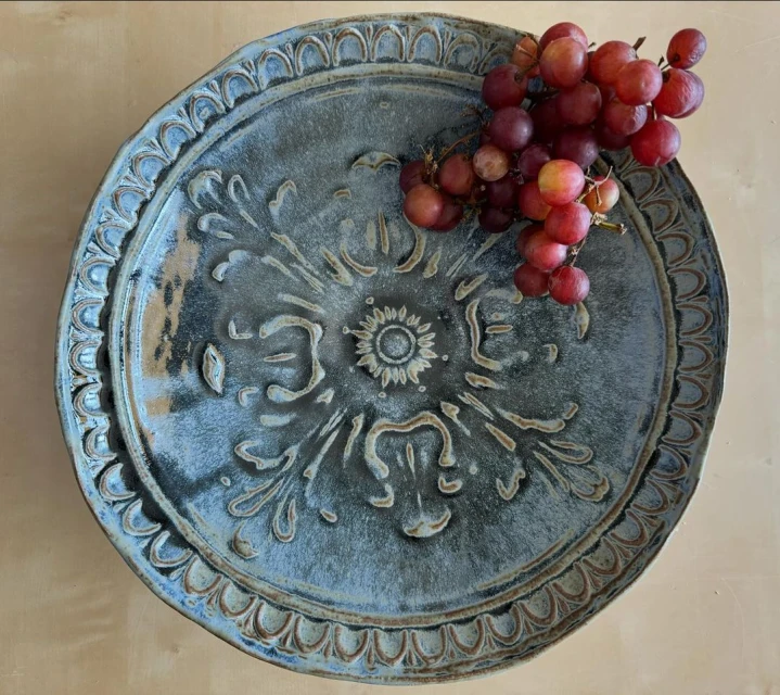 Artisan-crafted plate with ornate floral design, paired with a vibrant bunch of red grapes, creates a sophisticated food presentation.