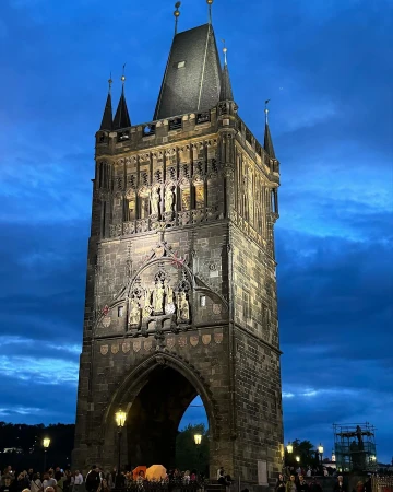 Nighttime view of the Old Town Bridge Tower in Prague, showcasing its architectural details and illuminated facade against a deep blue sky.