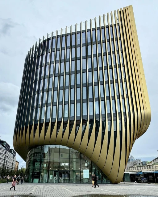 Exterior of the modern iSTYLE building featuring curved gold cladding, many windows, and urban setting on a cloudy day.