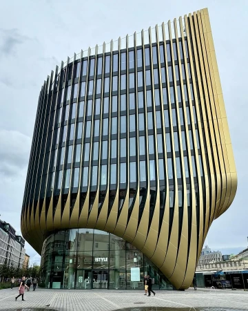 Exterior of the modern iSTYLE building featuring curved gold cladding, many windows, and urban setting on a cloudy day.