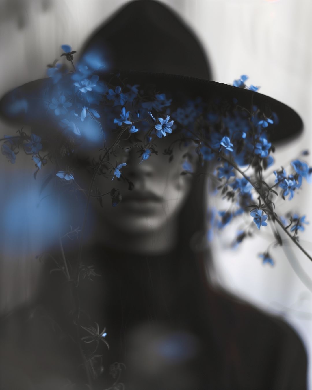Portrait of a woman wearing a wide-brimmed black hat obscured by out-of-focus blue flowers in the foreground.