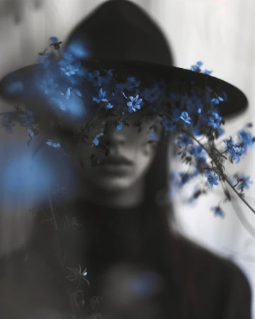 Portrait of a woman wearing a wide-brimmed black hat obscured by out-of-focus blue flowers in the foreground.