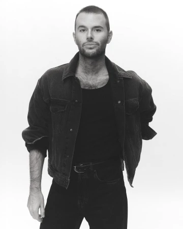 Portrait of a man with short hair wearing a dark denim jacket and t-shirt against a plain white background