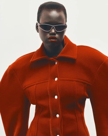 Model wearing dark futuristic sunglasses and a structured red jacket against a white background