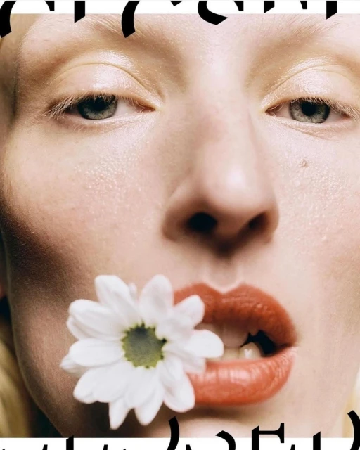 Close-up of a woman's face with red lips and a white daisy flower in her mouth, fair skin, and light hair. Beauty and fashion shot.