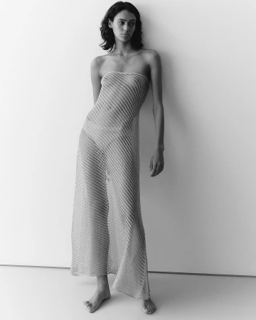 Monochrome portrait of a woman wearing a sheer ribbed strapless dress standing against a plain light wall