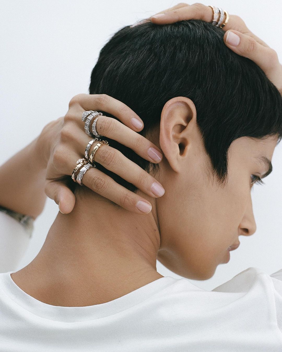 Close-up shot of a woman with short hair wearing multiple rings on her fingers, captured in a bright, clean studio environment.
