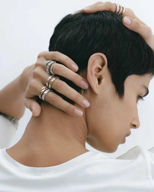 Close-up shot of a woman with short hair wearing multiple rings on her fingers, captured in a bright, clean studio environment.