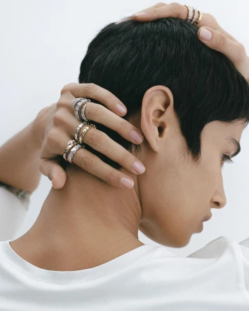 Close-up shot of a woman with short hair wearing multiple rings on her fingers, captured in a bright, clean studio environment.