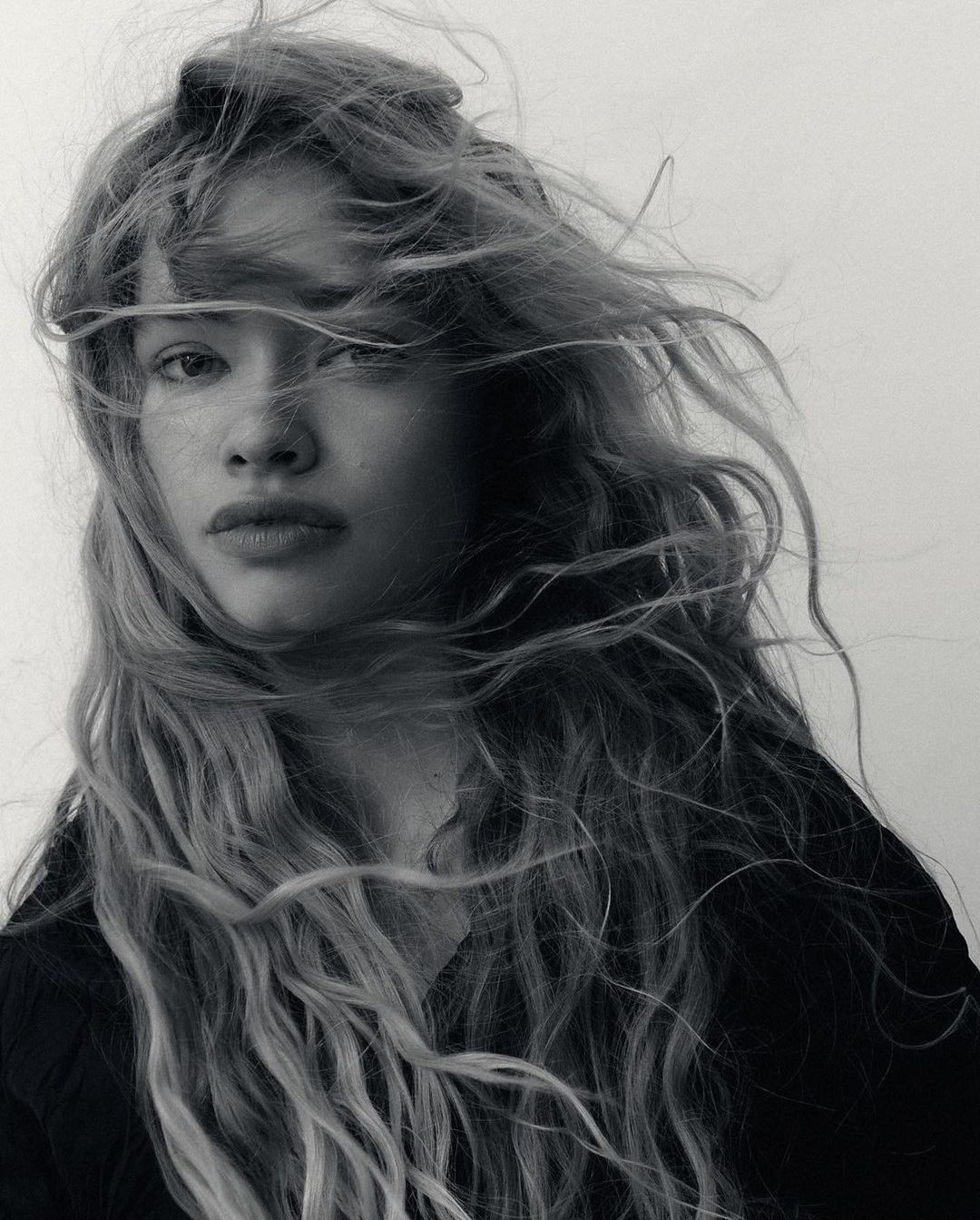 Black and white portrait of a young adult female with long wavy hair blowing in the wind against a neutral background. Beauty shot.