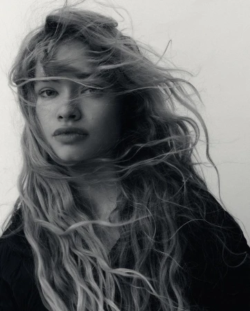 Black and white portrait of a young adult female with long wavy hair blowing in the wind against a neutral background. Beauty shot.
