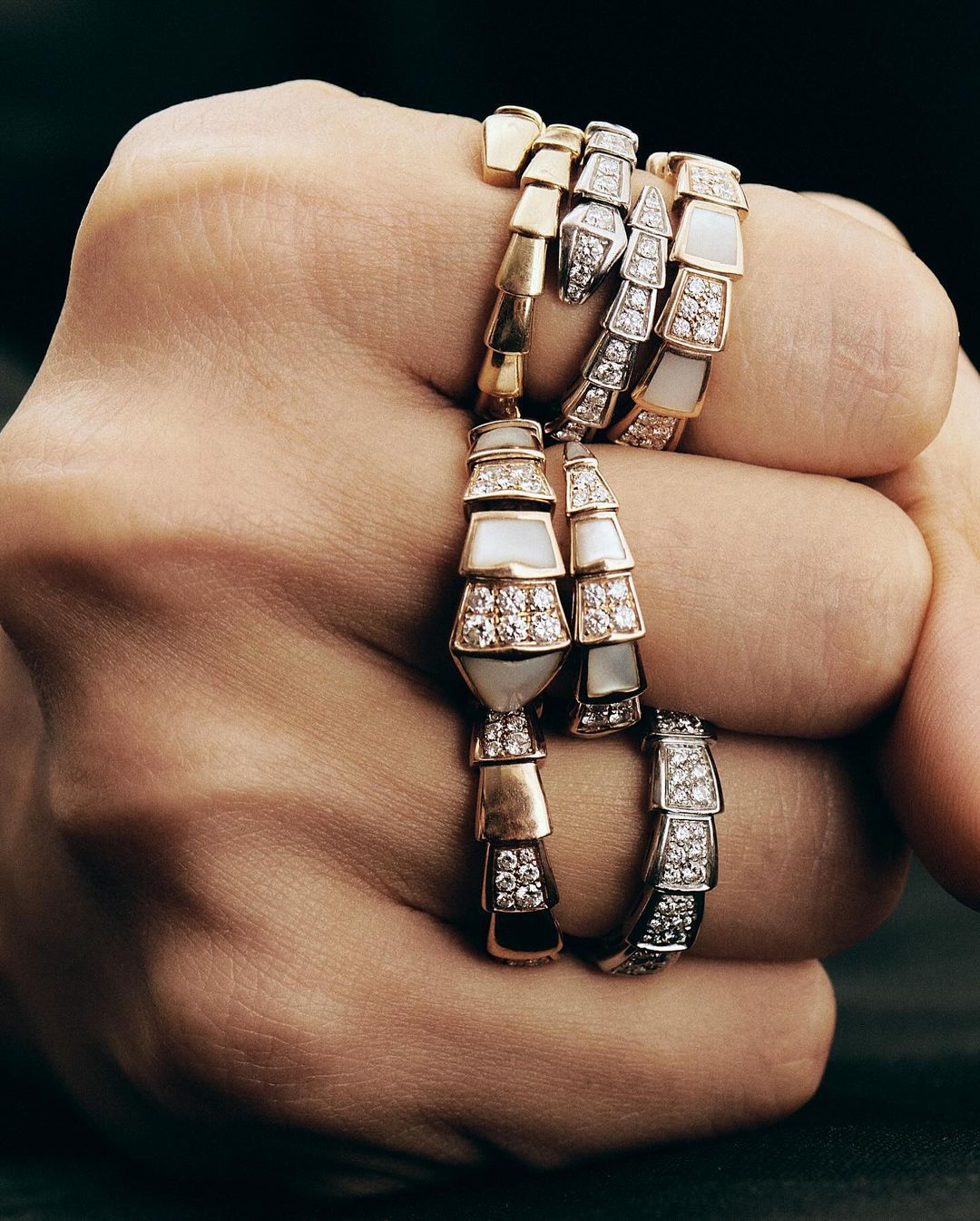 Close-up of a clenched fist adorned with several articulated snake rings in gold, silver, and diamond designs by Anna Daki.