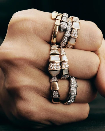 Close-up of a clenched fist adorned with several articulated snake rings in gold, silver, and diamond designs by Anna Daki.