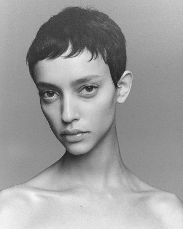 Black and white portrait of a woman with short pixie haircut and bangs looking directly at the camera