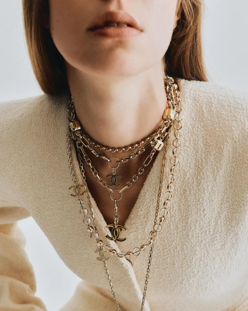Close-up of a woman wearing layered gold Chanel necklaces, showcasing fashion jewelry and the brand's iconic logo.
