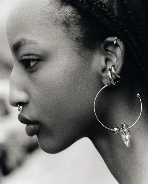 Profile view of an adult female with dark hair in braids, wearing various piercings and a large hoop earring with a crystal accent.