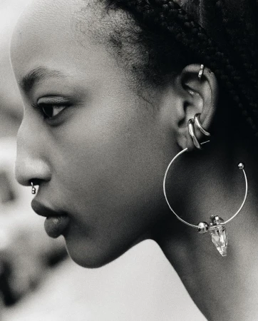 Profile view of an adult female with dark hair in braids, wearing various piercings and a large hoop earring with a crystal accent.
