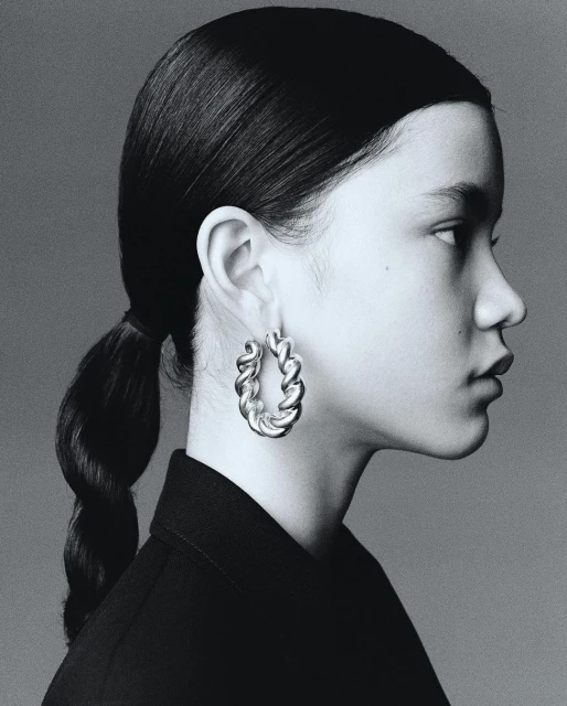 Profile portrait of an adult female with braided hair wearing hoop earrings and a dark top against a grey background. Studio shot.