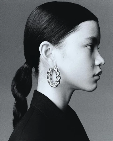 Profile portrait of an adult female with braided hair wearing hoop earrings and a dark top against a grey background. Studio shot.