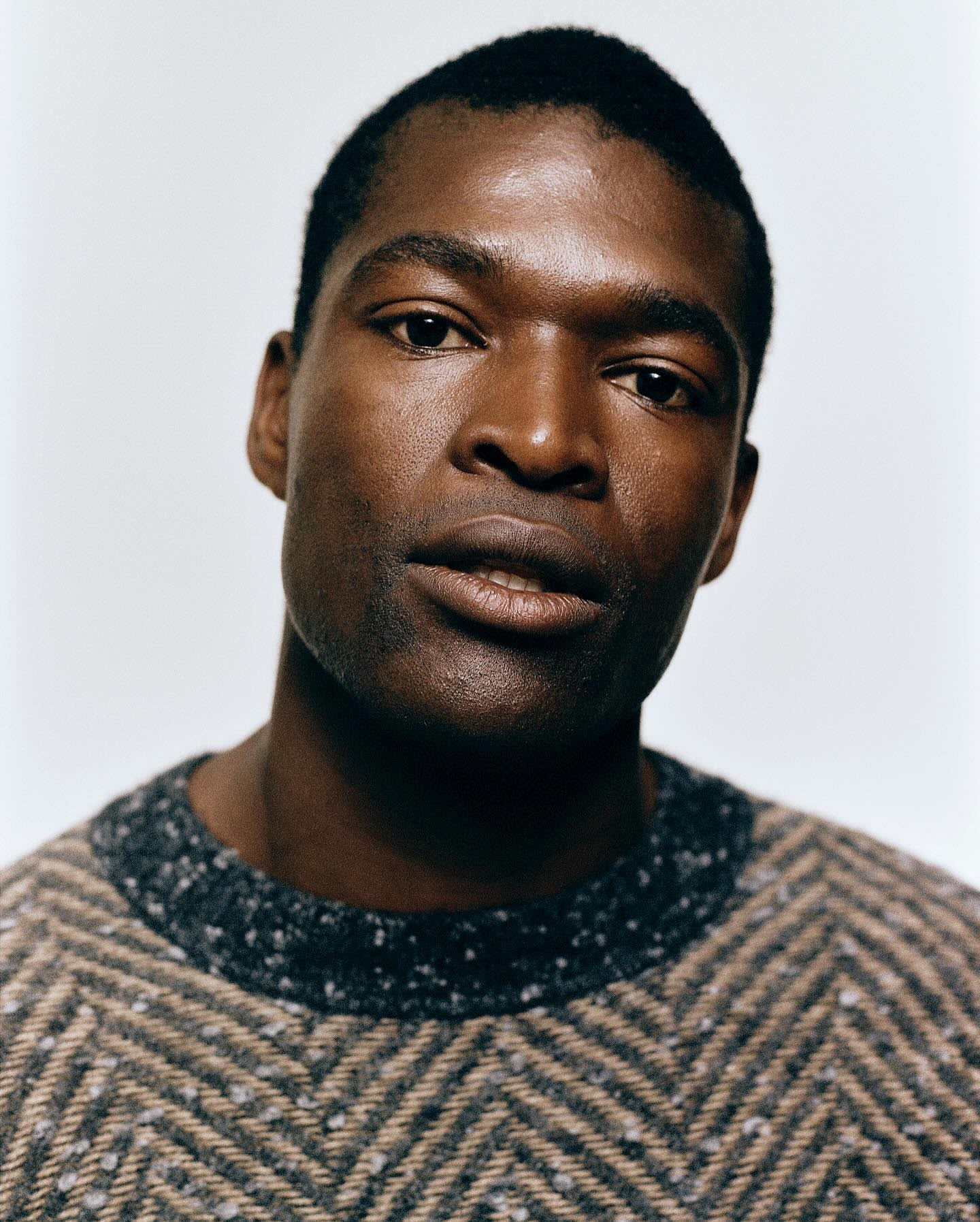 Portrait of an African American man with dark hair and a sweater, set against a plain background, showcasing textures and natural light.