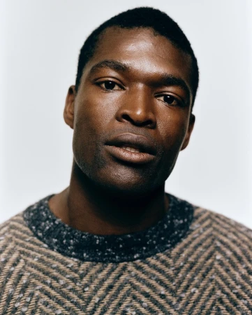 Portrait of an African American man with dark hair and a sweater, set against a plain background, showcasing textures and natural light.