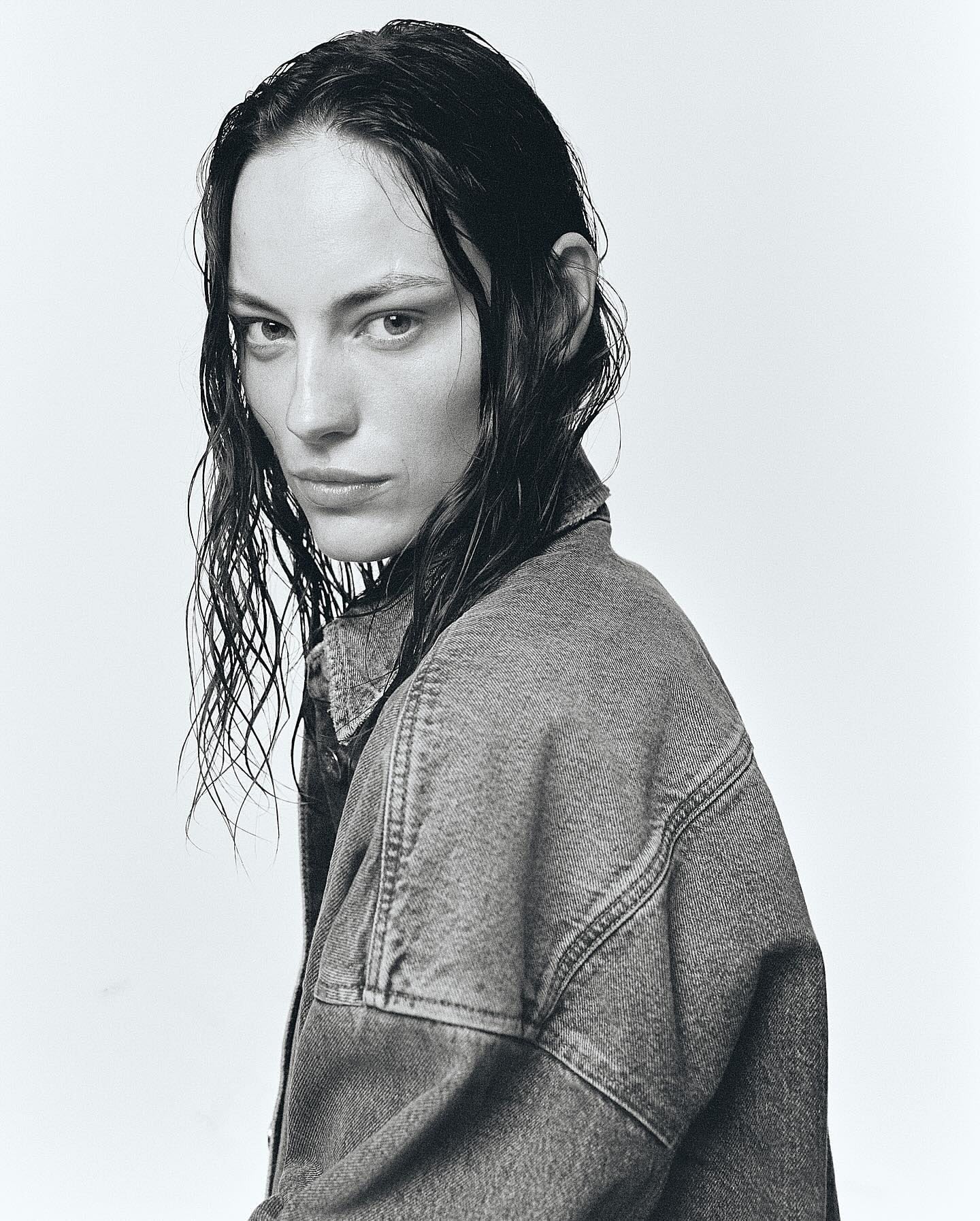 Monochrome portrait of a serious adult female with wet hair, wearing a denim jacket, set against a simple light background.