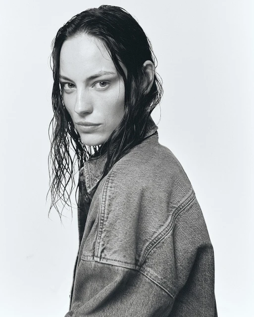 Monochrome portrait of a serious adult female with wet hair, wearing a denim jacket, set against a simple light background.