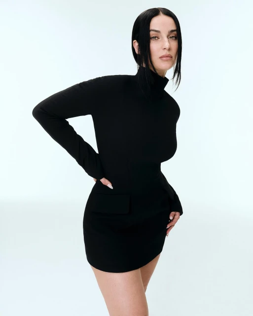 Elegant adult woman in black turtleneck dress strikes a pose against a light background in a studio setting for fashion. 