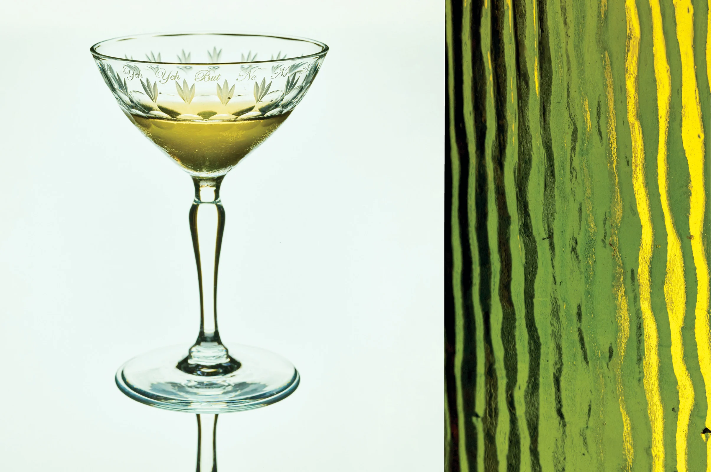 Elegant coupe glass filled with liquid against a textured green background creating a stylish, abstract still life composition.