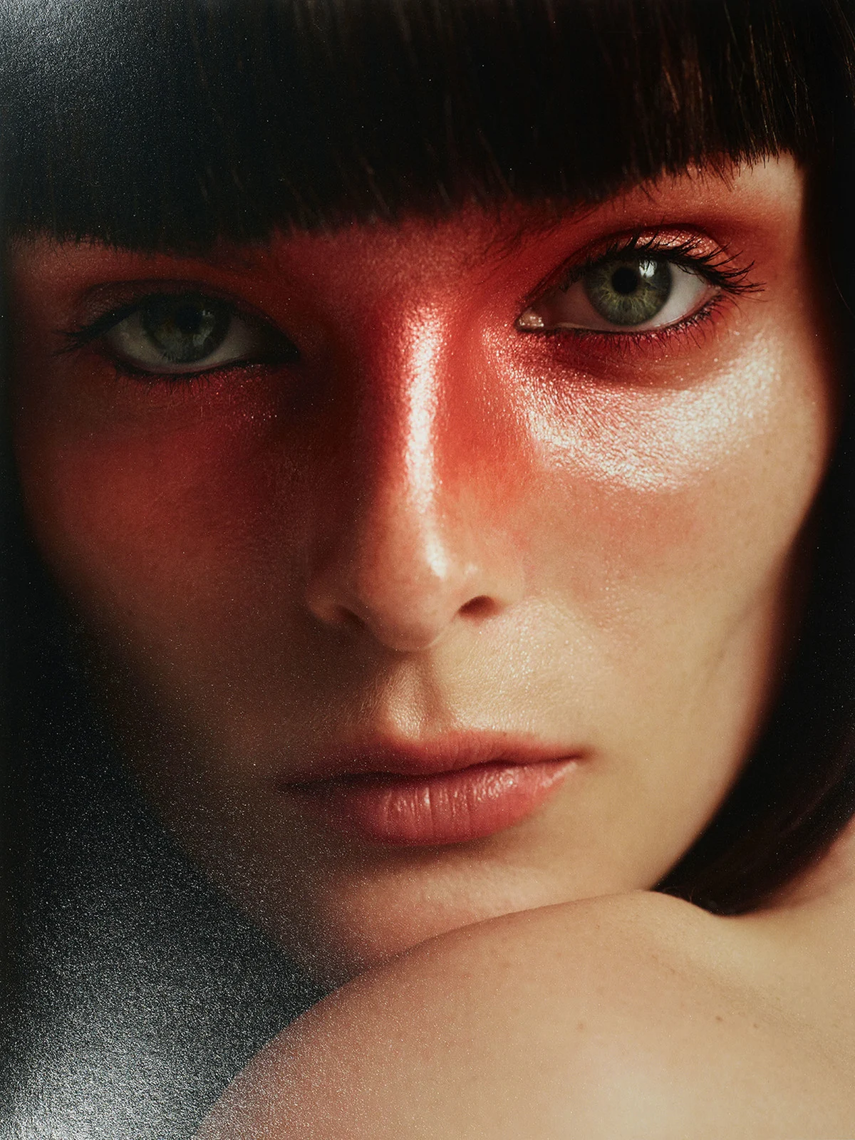 Close-up portrait of a woman with short dark hair, green eyes, fair skin, and red makeup on her forehead and cheeks.