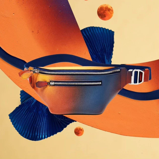 Studio shot of an orange and blue leather belt bag with metal hardware, floating against a split orange and beige background.