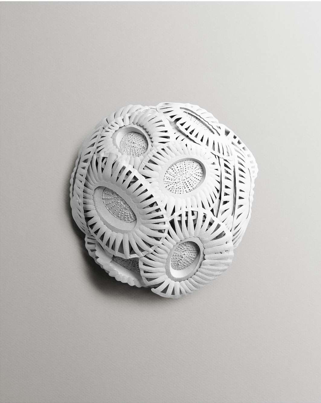 Detailed spherical art piece crafted from white material, featuring intricate laser-cut patterns, presented against a neutral background.