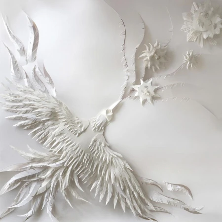 Intricate white paper sculpture of a bird in flight with layered feathers and floating star-like floral elements on white background.