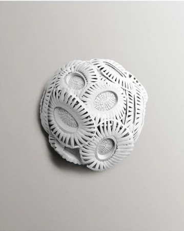 Intricate white paper sculpture with layered circular patterns set against a plain light grey gradient background.