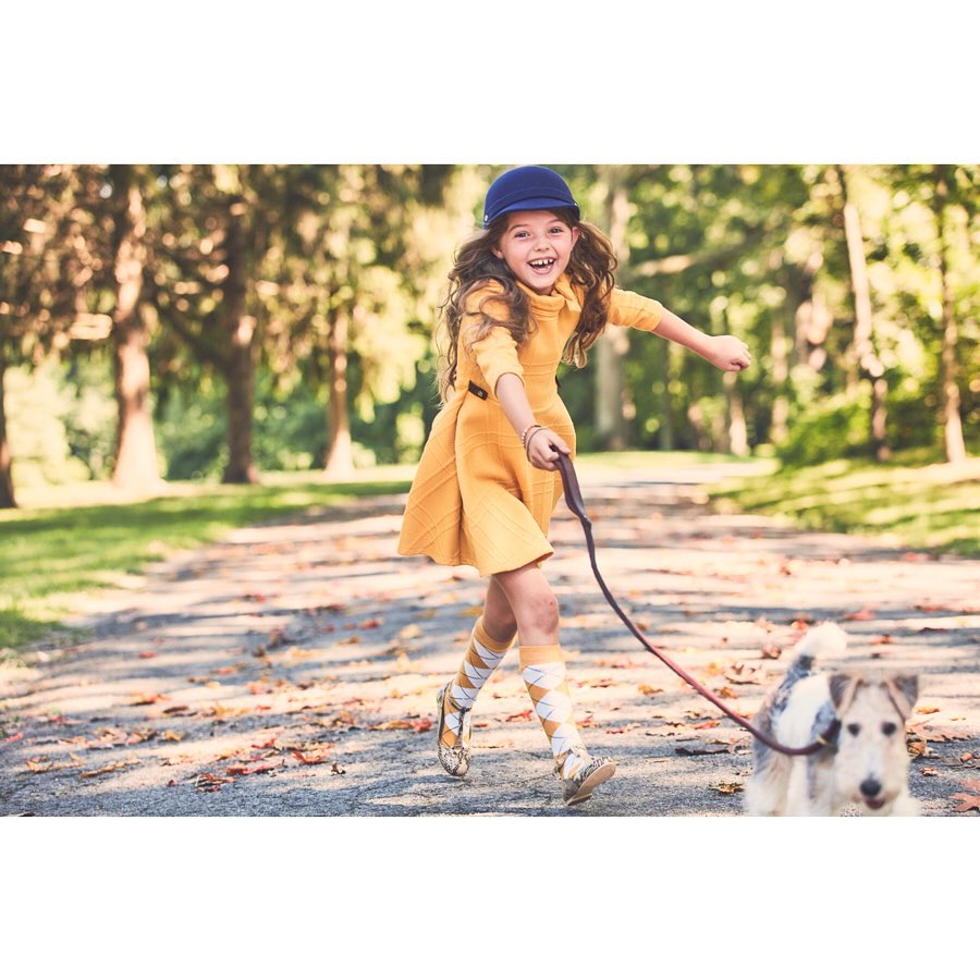 Young girl smiles while walking a wire fox terrier dog along a path in a sunny wooded area with tall trees.